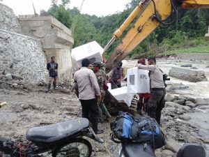 Anggota Polres Sumbawa Naiki Bucket Excavator Angkut Logistik Pilkada Seberangi Sungai di Orong Telu